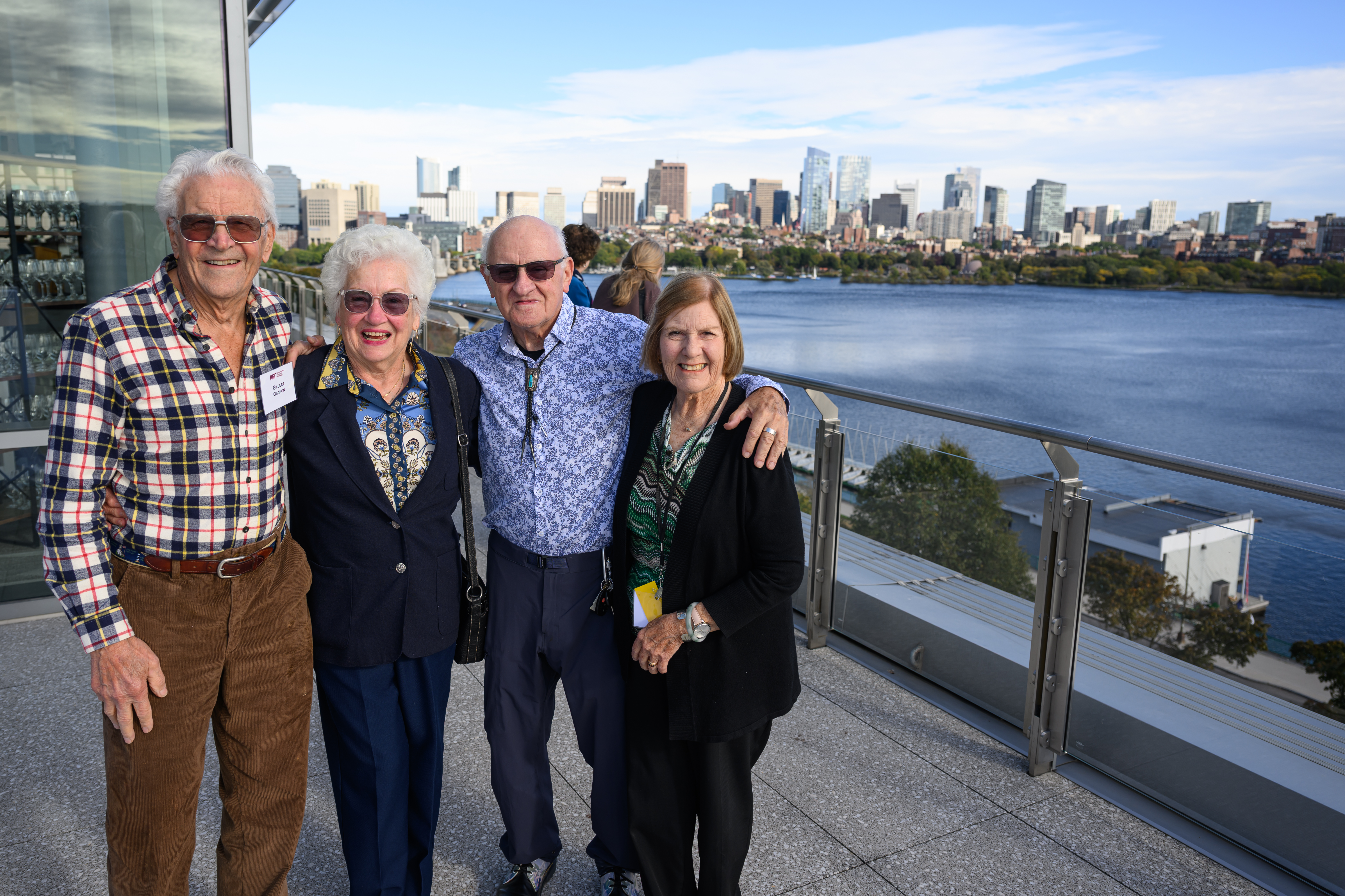 Gilbert Gagnon, Gloria Lucas, Hank Zeuli, and Terri Coyle with big smiles stand outside in front of a view of Boston's skyline