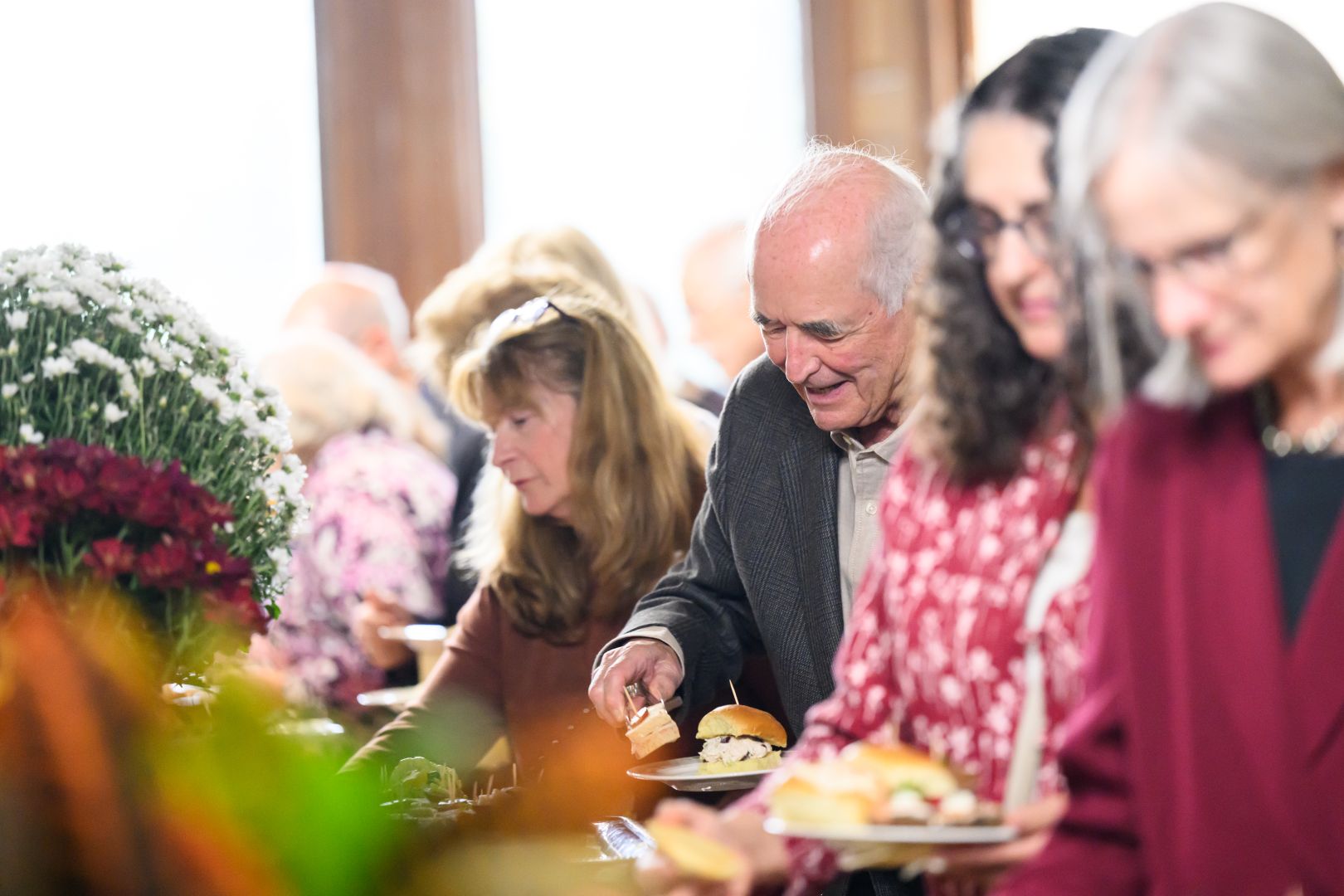QCC members in a buffet line filling their plates with an assortment of finger sandwiches